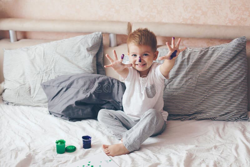 2 years old little boy dressed in pajamas is painting in the bed. 2 years old little boy dressed in pajamas is painting in the bed