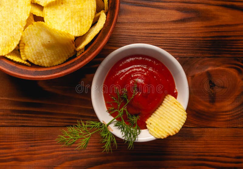 Așchii de cartofi ondulați într-o placă cu ketchup pe o masă din lemn. vedere de sus a gustărilor. chipsuri de cartofi pentru foto stock image