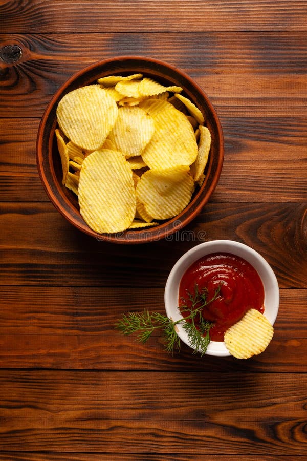 Așchii de cartofi ondulați într-o placă cu ketchup pe o masă din lemn. vedere de sus a gustărilor. chipsuri de cartofi pentru foto royalty free stock photography