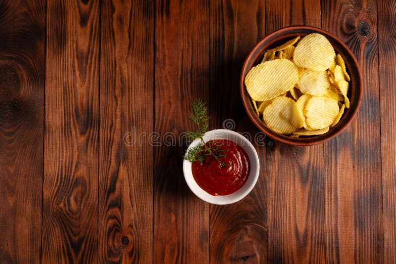 Așchii de cartofi ondulați într-o placă cu ketchup pe o masă din lemn. vedere de sus a gustărilor. chipsuri de cartofi pentru foto stock images