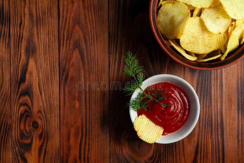 Așchii de cartofi ondulați într-o placă cu ketchup pe o masă din lemn. vedere de sus a gustărilor. chipsuri de cartofi pentru foto stock image