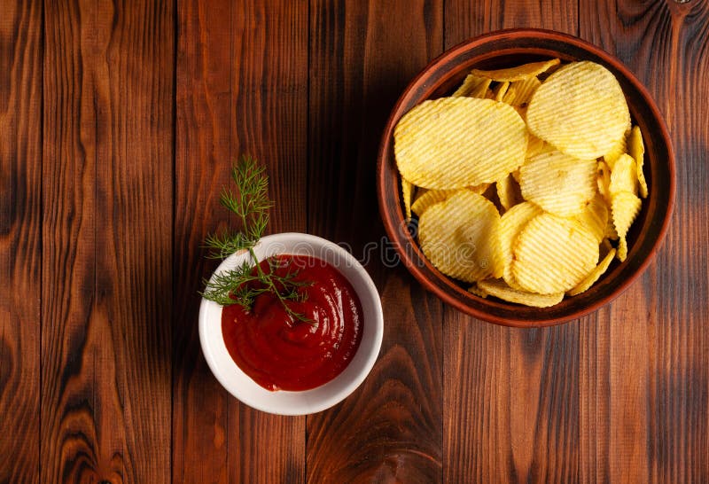 Așchii de cartofi ondulați într-o placă cu ketchup pe o masă din lemn. vedere de sus a gustărilor. chipsuri de cartofi pentru foto royalty free stock image