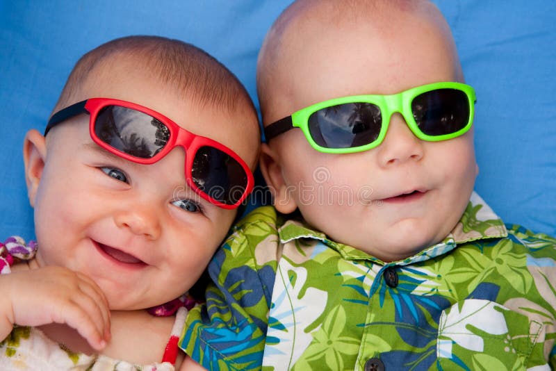 Due bambini in vacanza ai tropici, indossando occhiali da sole e sorridente (cinque e tre mesi di età)