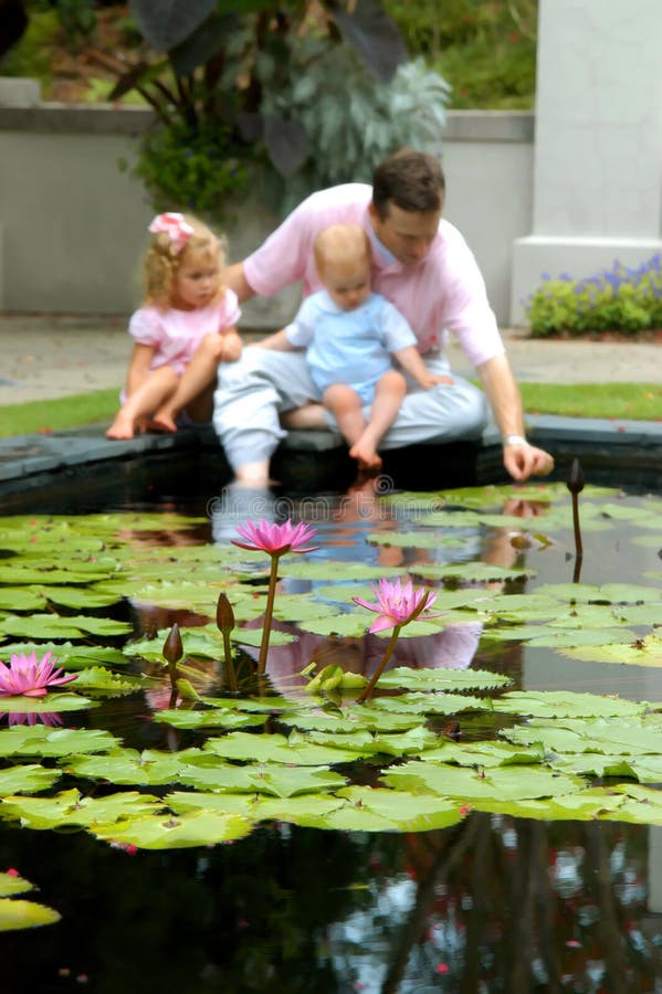 Family sit in dreamy background behind a pool filled with water lilies. Family sit in dreamy background behind a pool filled with water lilies.