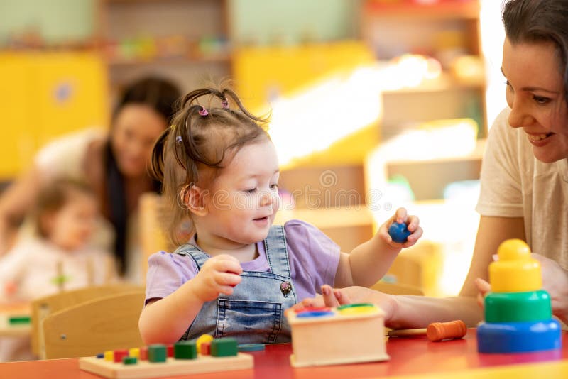 Babies with teachers play with developmental toys in nursery