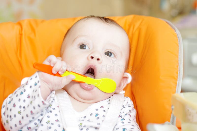 Baby Age of 5 Months with a Spoon Sits on a Babies Chair Stock Photo