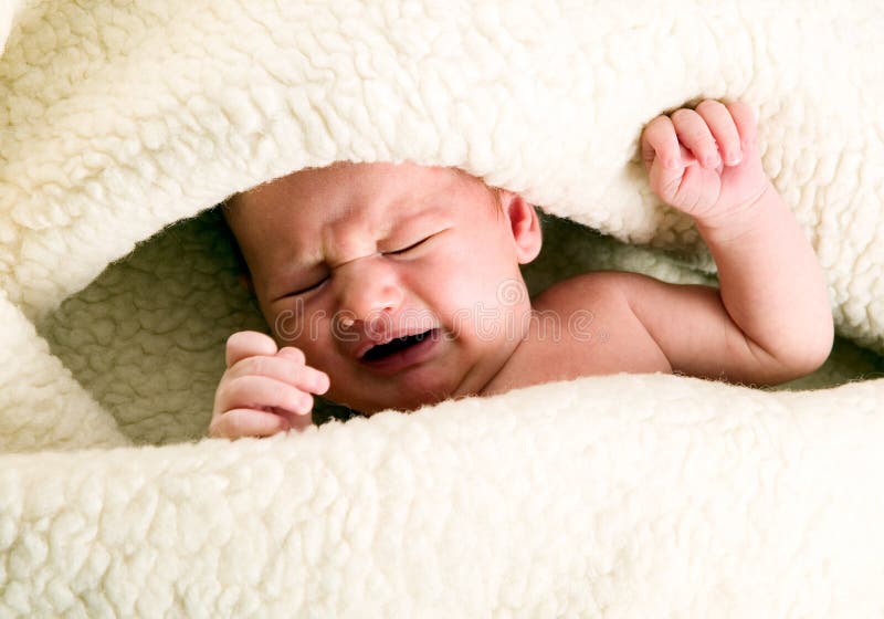 Baby boy is lying under blanket and cries royalty free stock image