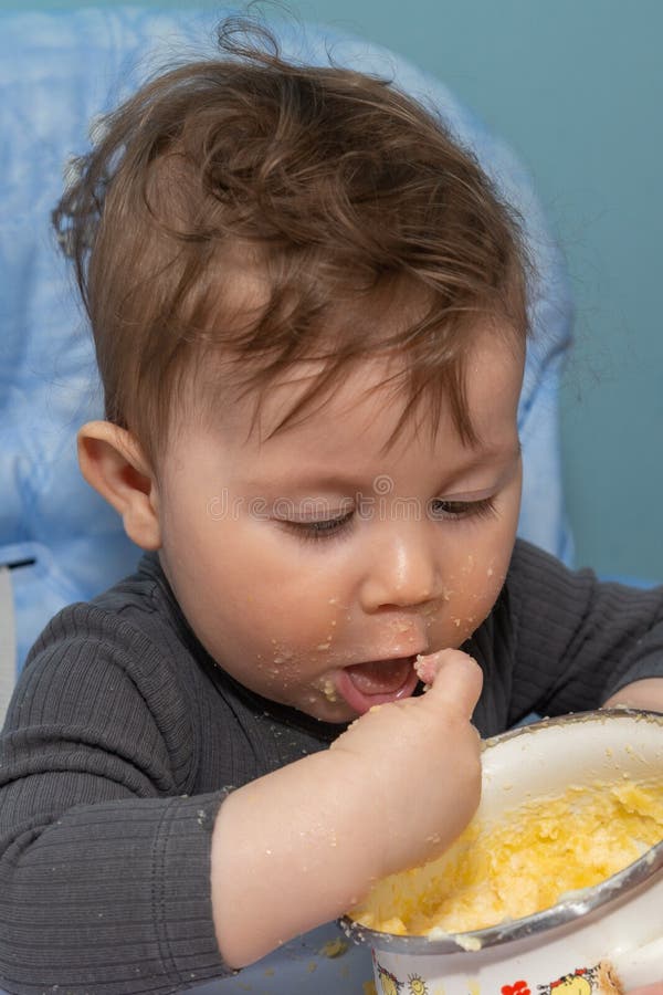 The Baby Boy is Sitting and Eating a Polenta with His Hands Stock Photo