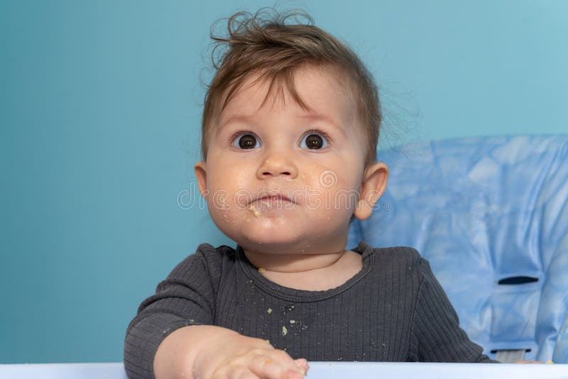 The Baby Boy is Sitting and Eating a Polenta with His Hands Stock Photo