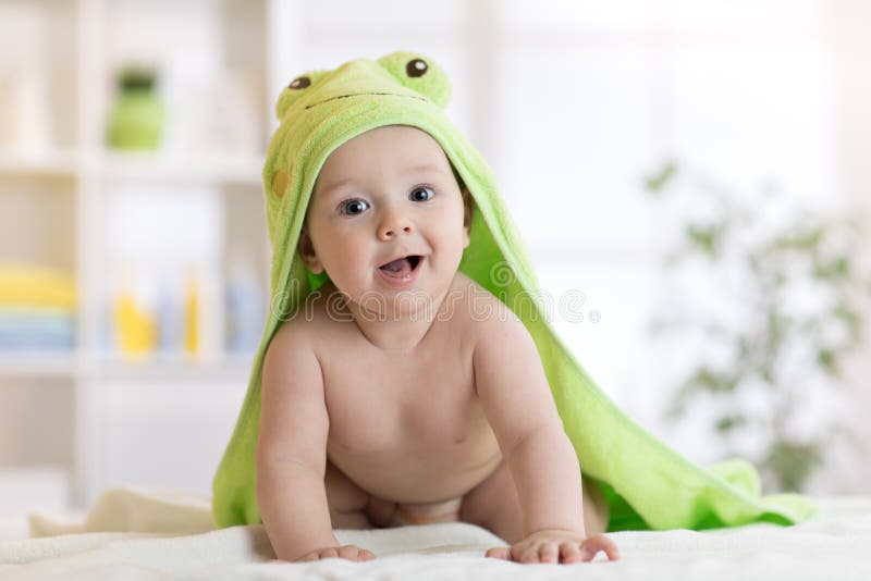 Baby boy wearing green towel in sunny bedroom. Newborn child relaxing after bath or shower.