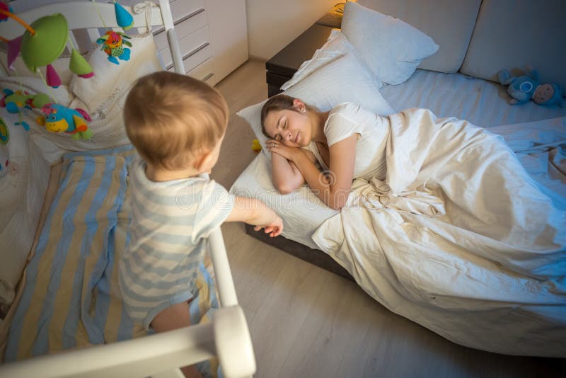 Baby in crib crying and trying to wake up mother that fell asleep stock images Baby in crib crying and trying to wake up mother that fell asleep stock images