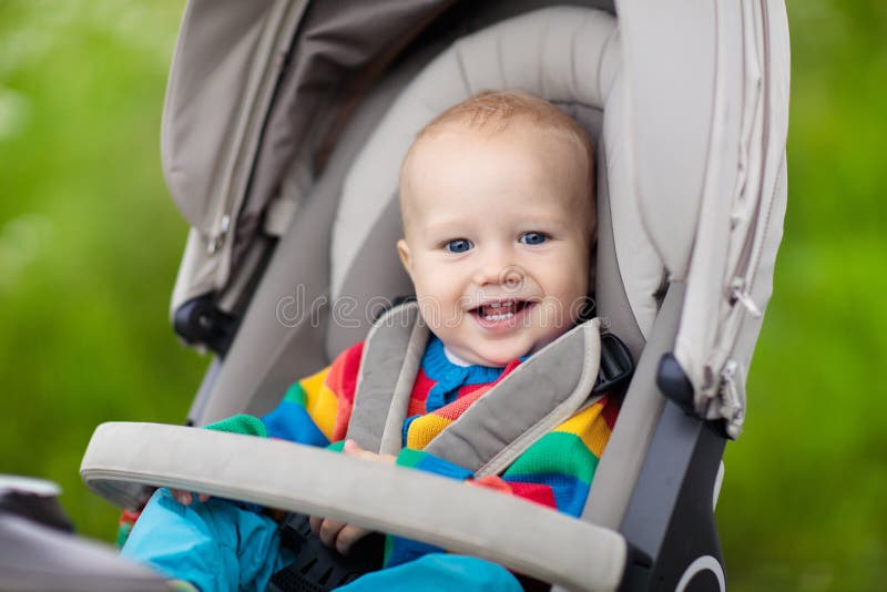 Baby in der warmen bunten gestrickten Jacke, die im modernen Spaziergänger auf einem Weg in einem Park sitzt Kind im Buggy Kleink lizenzfreies stockbild
