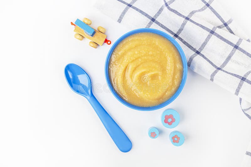 Baby food. Fresh homemade applesauce. Blue bowl with fruit puree on fabric and kids toys on table. The concept of proper nutrition