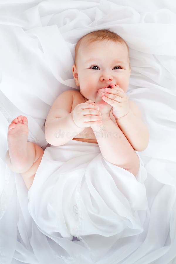 Baby girl lying on white fabric and holding legs royalty free stock photo Baby girl lying on white fabric and holding legs royalty free stock photo