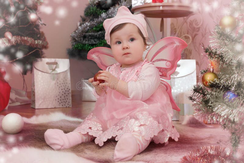 Baby girl with pink butterfly wings sitting under Christmas tree