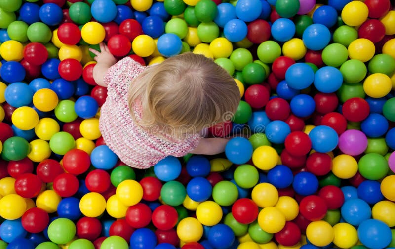 Baby girl playing in playground colourful ball pool. Closup overview