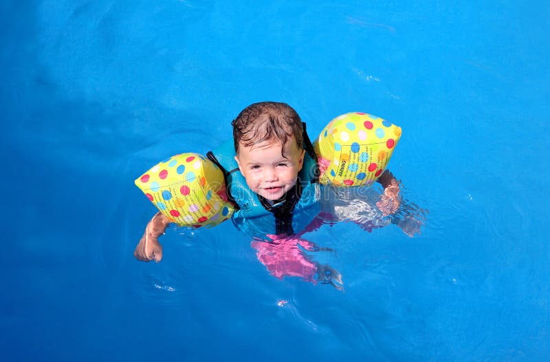 Bambina galleggiante sulla parte superiore della piscina in galleggiamento giacca e bande di braccio.