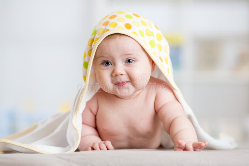 Baby girl wrapped towel in children nursery room. Newborn kid relaxing in bed after bath or shower.