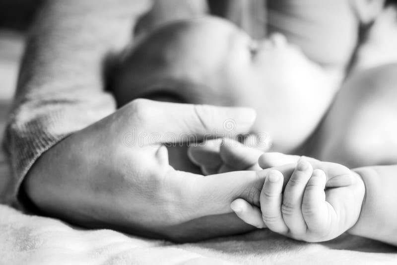 The baby is holding on to the mother`s finger. Hands close-up. Black and white photo. Side view. Concept of motherhood and