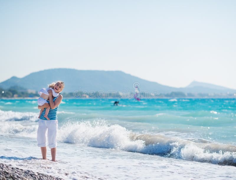 Baby hugging happy young mother standing at sea shore. Baby hugging happy young mother standing at sea shore