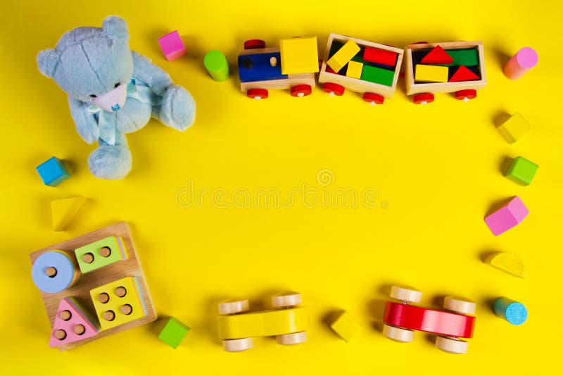 Baby kids toys background. Teddy bear, wooden train, car, colorful wood toys and bricks on yellow background. Top view