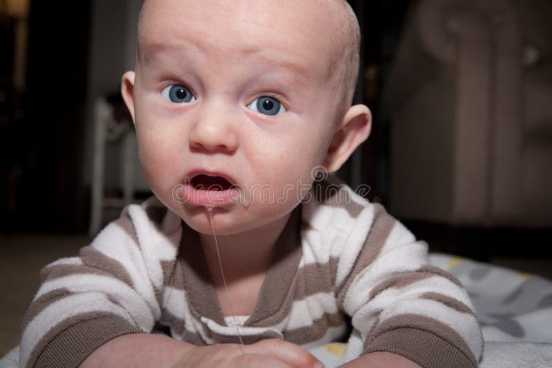 Baby with blue eyes lying on his stomach with drool hanging from his mouth. Image orientation is horizontal and there is copy space. Baby with blue eyes lying on his stomach with drool hanging from his mouth. Image orientation is horizontal and there is copy space.