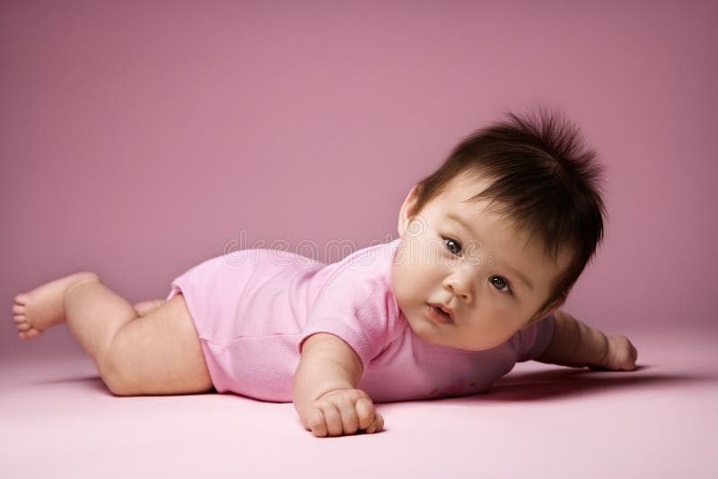 Baby lying on stomach looking at viewer. Asian baby lying on stomach looking at viewer holding arms out to side Baby lying on stomach looking at viewer. Asian baby lying on stomach looking at viewer holding arms out to side