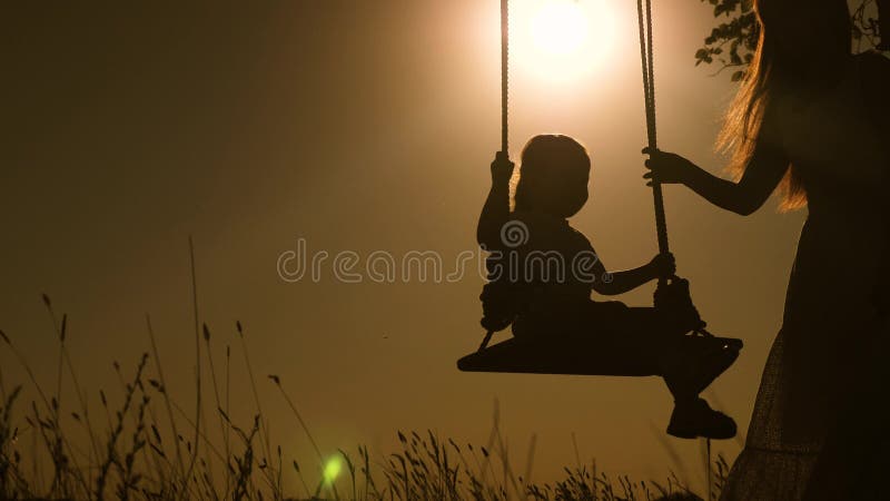 Baby and mom swinging on a swing in park in sun. silhouette of small healthy child on swing. daughter and mother love