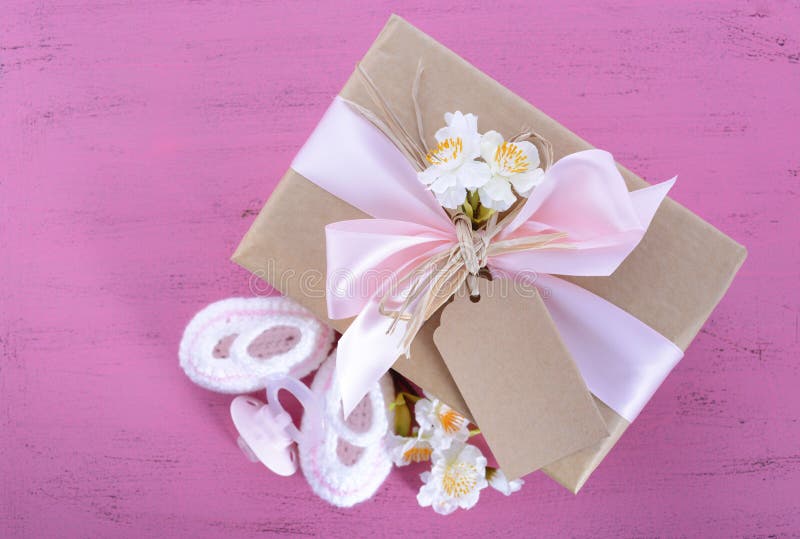 Baby shower Its a Girl natural wrap gift with gift box, baby booties and dummy on pink shabby chic rustic wood table.