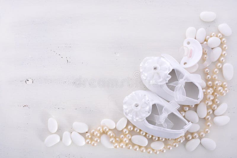 Baby shower neutral white background with baby booties, pearls, and sugar almonds on shabby chic rustic wood table, with copy space. Baby shower neutral white background with baby booties, pearls, and sugar almonds on shabby chic rustic wood table, with copy space.