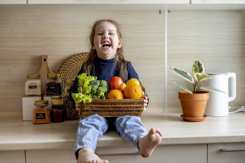Baby sits on the kitchen table and holds a wicker basket of fruit in her hands stock images