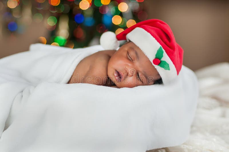 A baby sleeping comfy in blanket and Santa hat under colourful Christmas lights