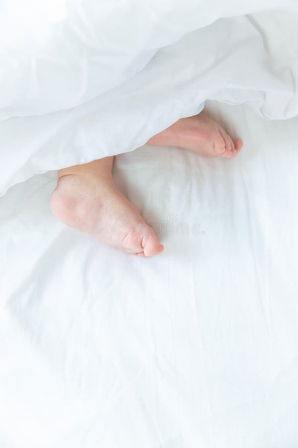 Baby Sleeps on a White Bed with His Feet. Selective Focus Stock Photo