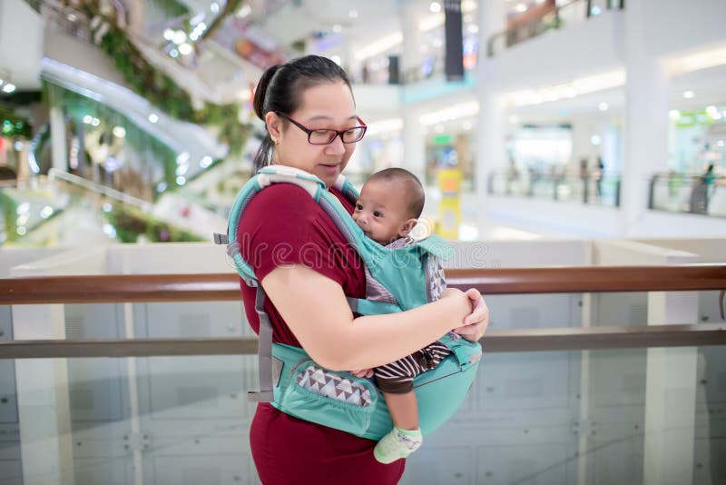 Baby in sling indoor. Little baby boy and her mother walking in department store. stock photography Baby in sling indoor. Little baby boy and her mother walking in department store. stock photography