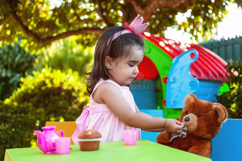 Baby toddler girl playing in outdoor tea party feeding her best friend Teddy Bear with candy stock images Baby toddler girl playing in outdoor tea party feeding her best friend Teddy Bear with candy stock images