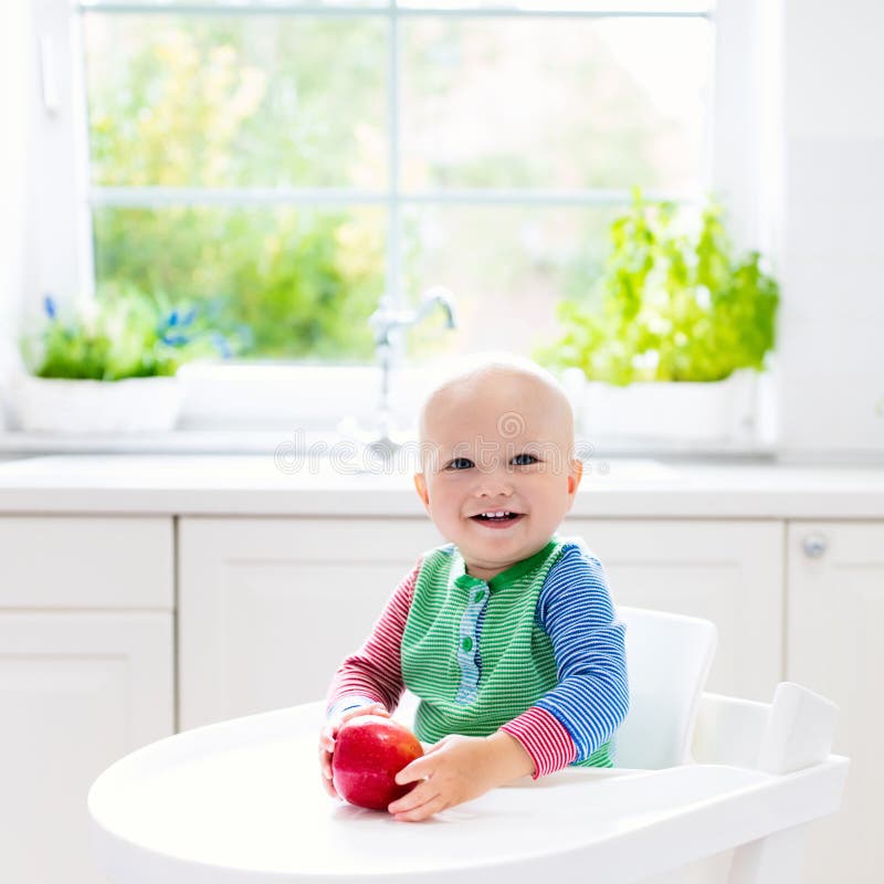 Babyjongen die appel in witte keuken thuis eten stock afbeelding Babyjongen die appel in witte keuken thuis eten stock afbeelding