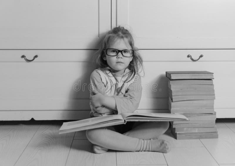 Babymeisje met boek en glazen die op de zwart-witte vloer zitten, stock foto Babymeisje met boek en glazen die op de zwart-witte vloer zitten, stock foto