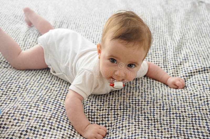 Babymeisje, vier maanden oud, op het bed met fopspeen stock fotografie Babymeisje, vier maanden oud, op het bed met fopspeen stock fotografie