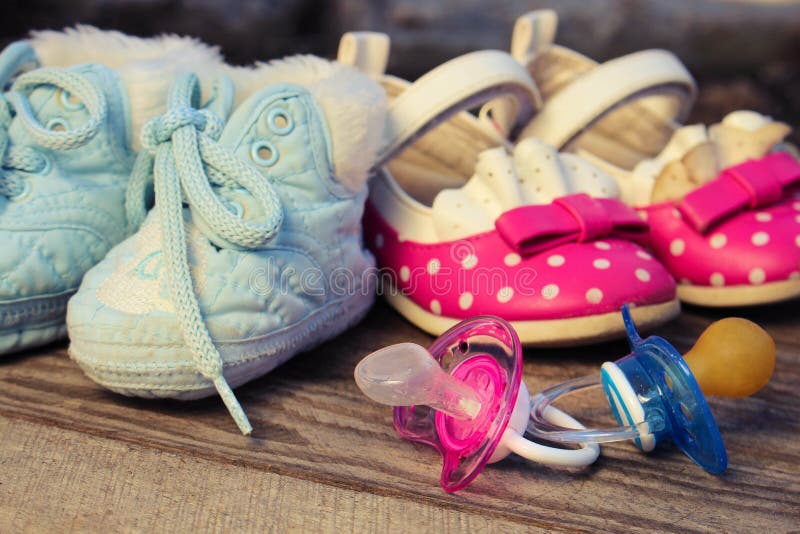 Baby shoes and pacifiers pink and blue on the old wooden background. Toned image. Baby shoes and pacifiers pink and blue on the old wooden background. Toned image.