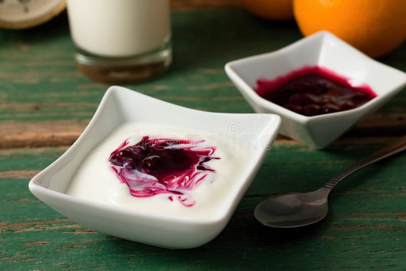 Bacca rossa in yogurt bianco disposto con la ciotola sulla tavola verde immagini stock Bacca rossa in yogurt bianco disposto con la ciotola sulla tavola verde immagini stock