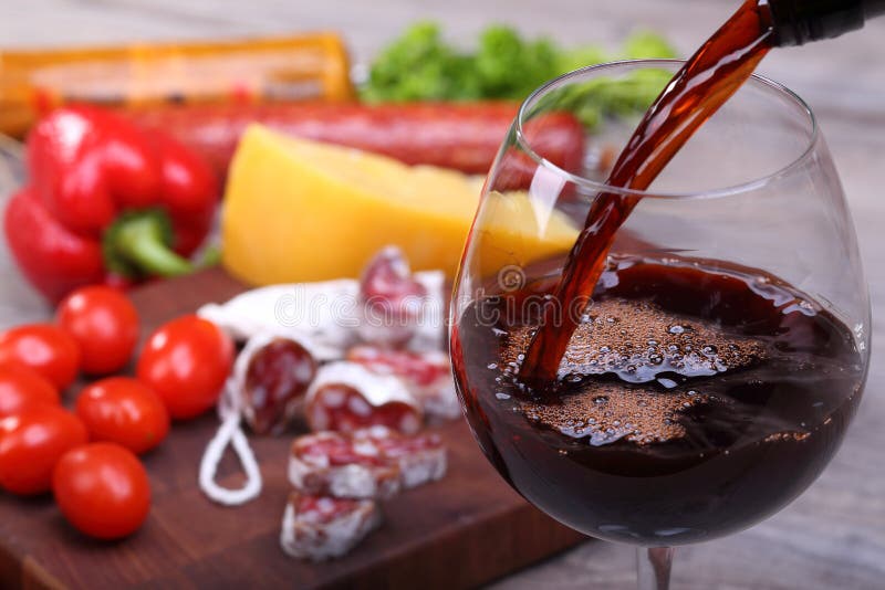 Pouring red wine into glass and food background. Pouring red wine into glass and food background