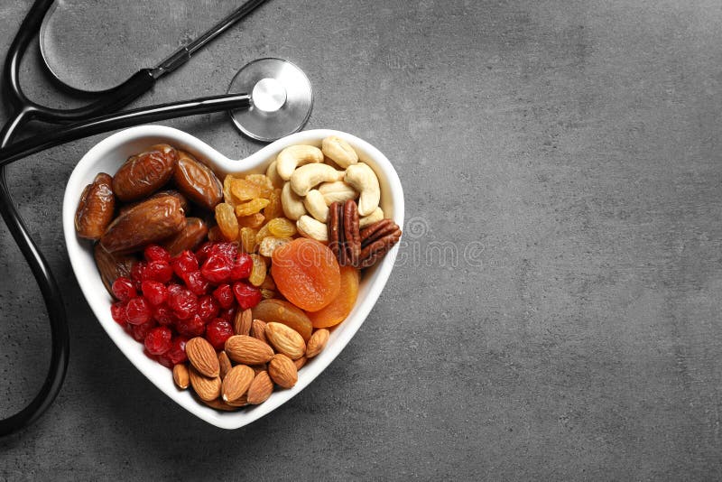 Heart shaped bowl with nuts and dried fruits near stethoscope on grey background, top view. Space for text. Heart shaped bowl with nuts and dried fruits near stethoscope on grey background, top view. Space for text