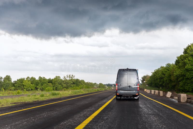 Back of delivery small shipment cargo courier van moving fast on wet highway road to city urban suburb against rainy. Cloudy sky . Business distribution and