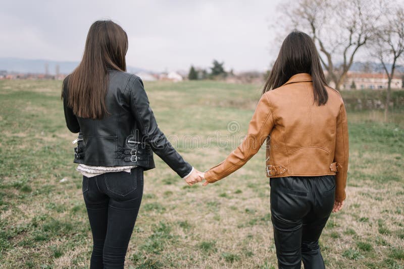 Back of girls holding hands in the park. Backview of two girls walking in nature with hands clasped in spring day.