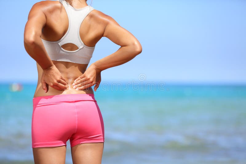 Back pain. Athletic woman in pink sportswear standing at the seaside rubbing the muscles of her lower back, cropped torso portrait. Back pain. Athletic woman in pink sportswear standing at the seaside rubbing the muscles of her lower back, cropped torso portrait.