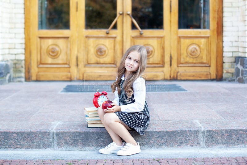 Back to school. Child little girl student sits on the steps near the school and holds an apple in her hands. Schoolgirl is having royalty free stock photos Back to school. Child little girl student sits on the steps near the school and holds an apple in her hands. Schoolgirl is having royalty free stock photos