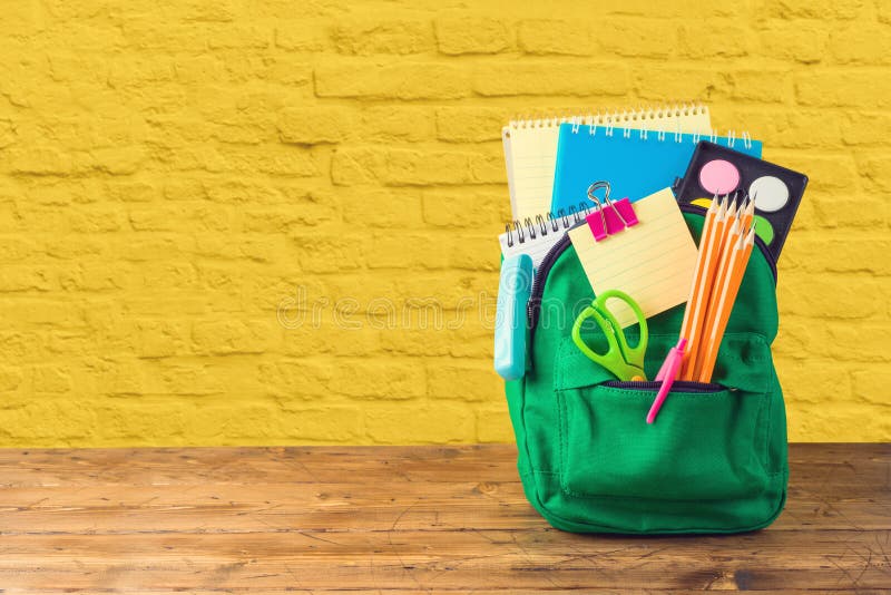 Back to school concept with bag backpack and school supplies on wooden table over yellow brick wall background