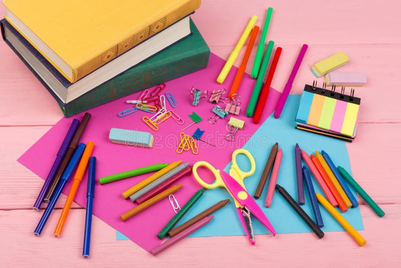 Back to school concept - school supplies: books, markers, crayons, pink and blue paper, scissors, eraser and other accessories on pink wooden table