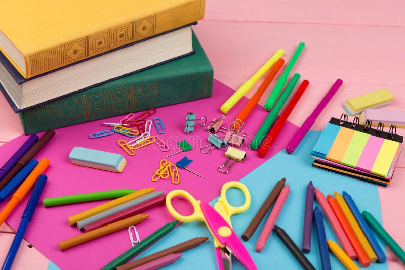 Back to school concept - school supplies: books, markers, crayons, pink and blue paper, scissors, eraser and other accessories on pink wooden table