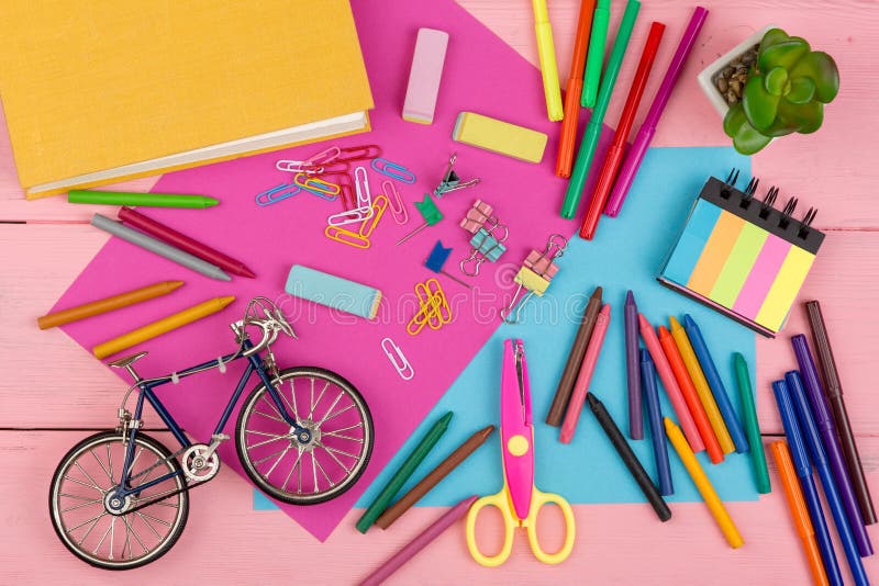 Back to school concept - school supplies: books, markers, crayons, pink and blue paper, scissors, eraser and other accessories on pink wooden table